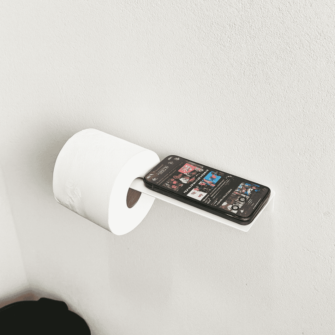 Porta papel higiênico branco com prateleira superior servindo de suporte para celular, acessório prático e moderno para banheiros.